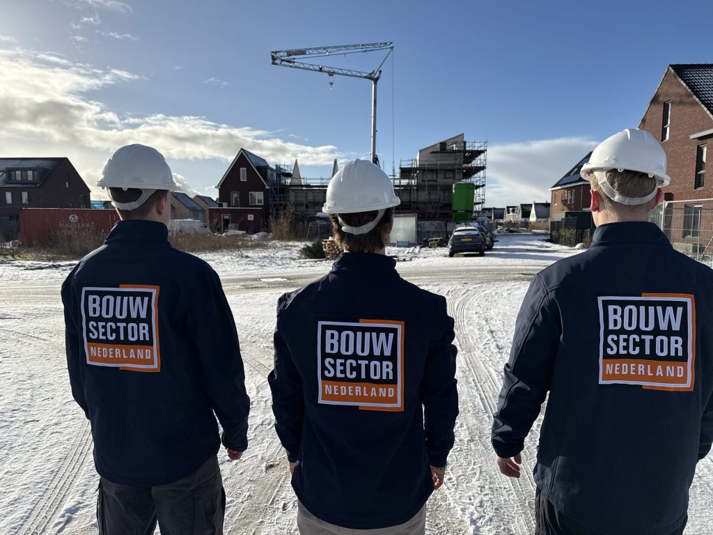 Drie vakmensen van Bouwsector Nederland met witte helm kijken naar nieuwe woningen in aanbouw